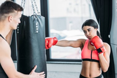 Erkek antrenör eğitim spor salonunda boks eldivenleri kum torbası ve Afro-Amerikan Kız holding