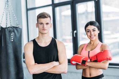 erkek eğitmen ve boks eldivengenç afrikalı amerikalı kadın birlikte ayakta ve spor salonunda kamera bakarak