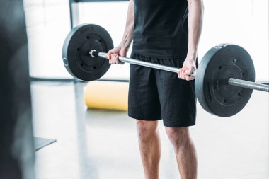 cropped shot of young man in sportswear lifting barbell in gym clipart