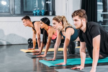 çok ırklı atletik genç erkek ve kadın yoga paspaslar üzerinde egzersiz ve spor salonunda uzağa bakıyor