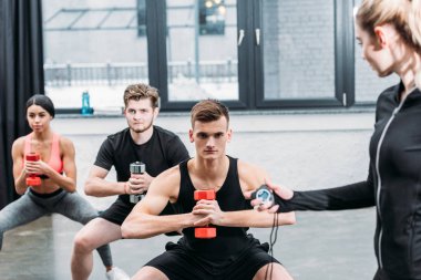 holding Zamanlayıcı ve sportif gençler spor salonunda dumbbells ile egzersiz eğitmen