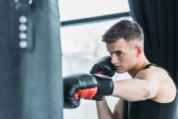 集中精神的年轻运动男子拳击与拳击袋在体育馆 — 图库照片