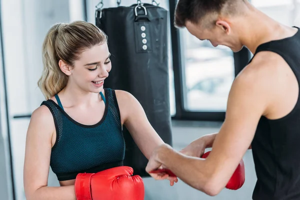 男性教练戴拳击手套对微笑的运动女孩在健身房 — 图库照片