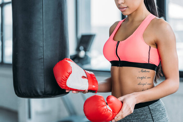 cropped shot of sporty african american girl holding boxing gloves in gym