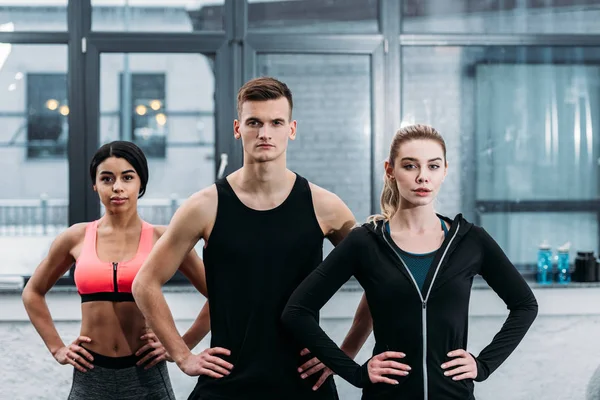 spor giyim atletik genç arkadaşlar bel elleri ile ayakta ve spor salonunda kamera bakarak
