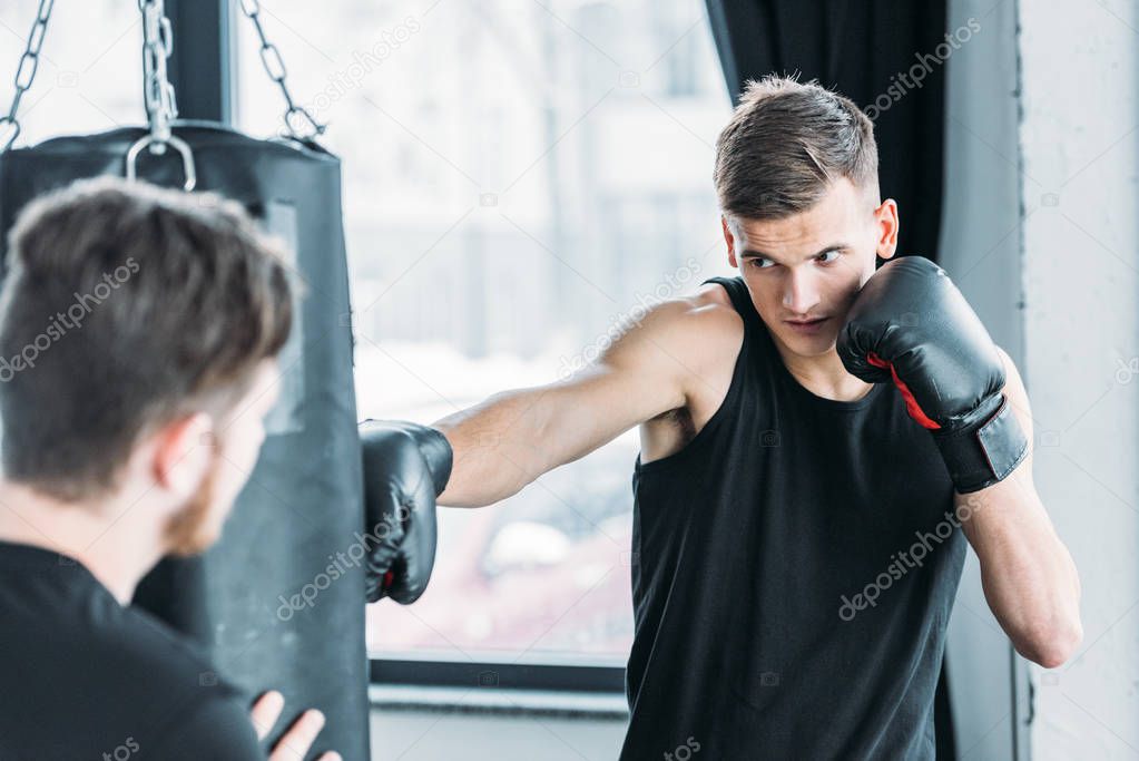 trainer holding punching bag and young man in boxing gloves training in gym