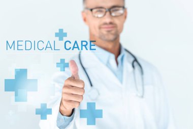 yakışıklı Doktor stetoskop tıbbi bakım yazı ile başparmak gösterilmesini omuzlarında ile bardaklarda seçici odak 