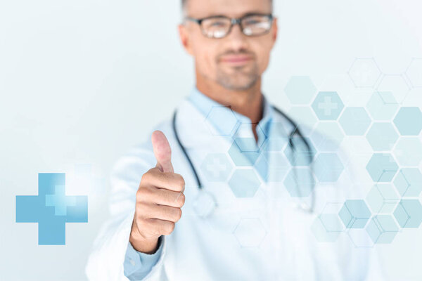 selective focus of handsome doctor in glasses with stethoscope on shoulders showing thumb up with medical interface