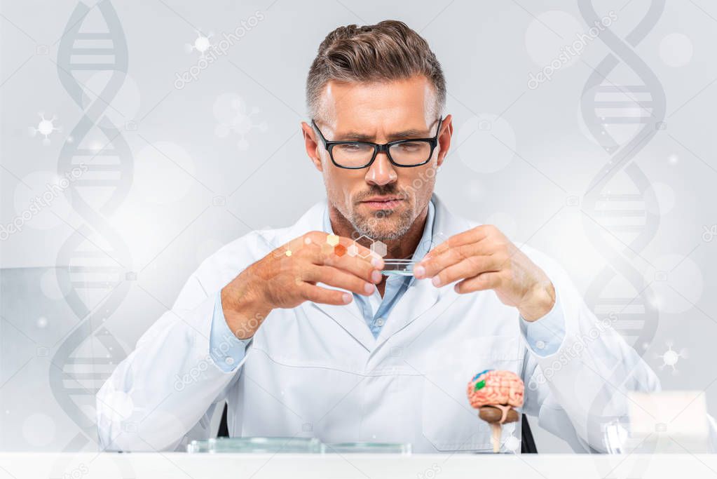 handsome scientist in glasses looking at reagent with dna symbols