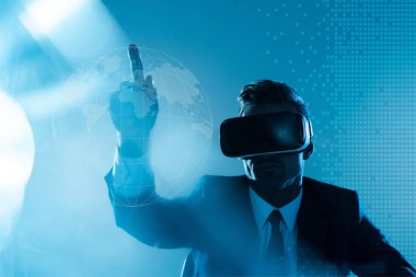businessman in virtual reality headset pointing on globe isolated on blue, artificial intelligence concept clipart