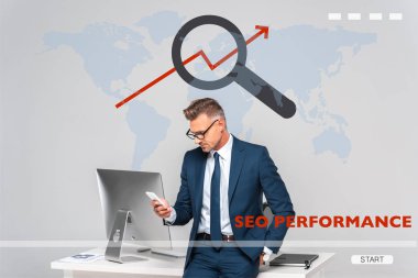 masanın üzerine eğilerek ve Grey dünya harita ve seo performans ile izole smartphone kullanarak yakışıklı işadamı 