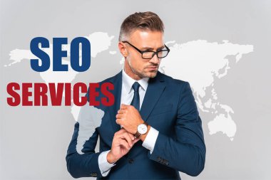handsome businessman wearing wristwatch and looking away isolated on grey with world map and seo services clipart