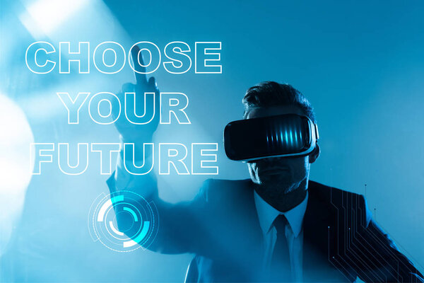 businessman in virtual reality headset pointing on "choose your future" lettering isolated on blue, artificial intelligence concept