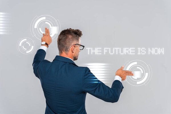 rear view of businessman in glasses touching something isolated on grey, artificial intelligence concept, "the future is now" lettering