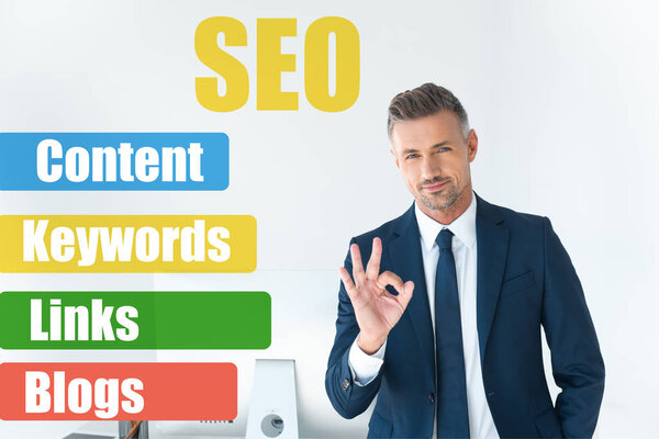 красивый бизнесмен, показывающий нормальный жест и смотрящий на камеру, изолированную на белом с символами SEO
