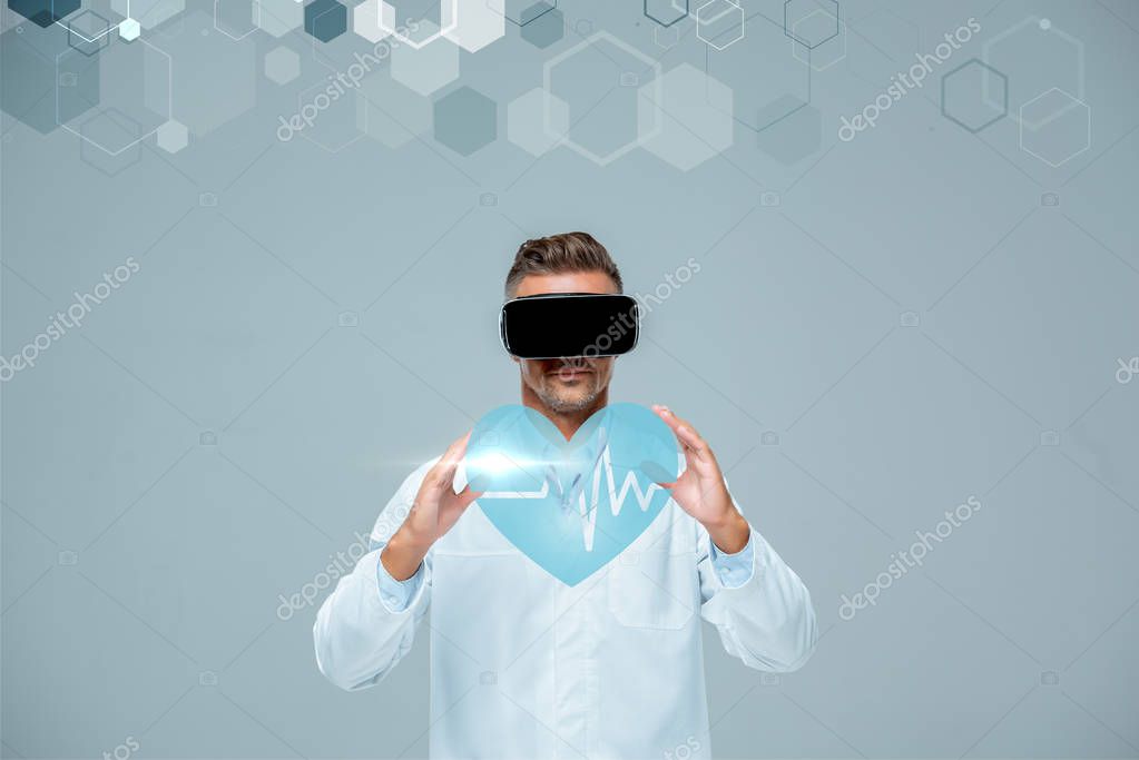 Scientist in virtual reality headset holding heart with heartbeat isolated on grey, artificial intelligence concept
