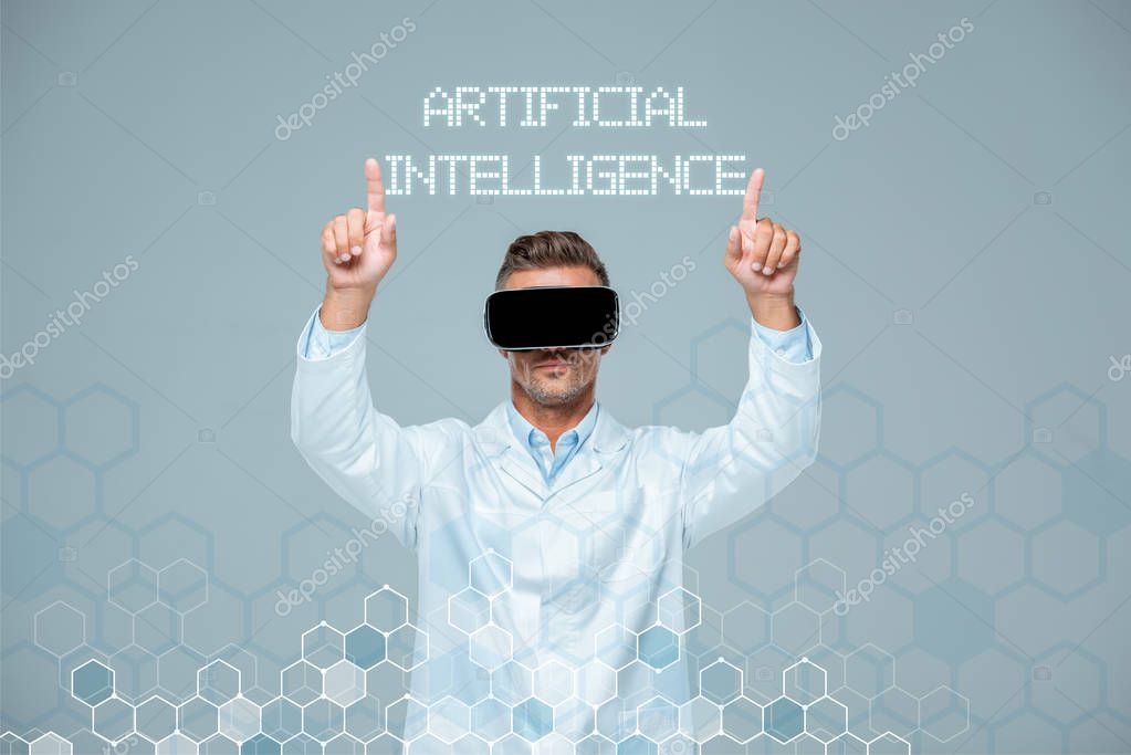 Scientist in virtual reality headset touching artificial intelligence lettering with two fingers isolated on grey