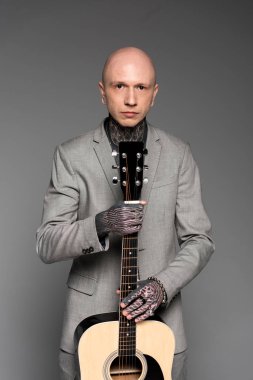 Akustik gitar tutarak ve gri izole kamera seyir uymak yakışıklı kel dövmeli adam