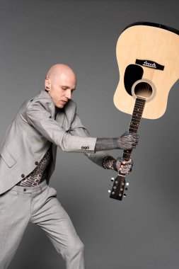 Akustik gitar gri izole isabet takım elbiseli kızgın dövmeli adam 