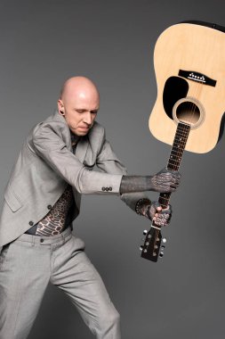 Akustik gitar gri izole isabet takım elbiseli agresif dövmeli adam  