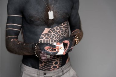 mid section of bare-chested man with tattoos holding cigarette box isolated on grey clipart