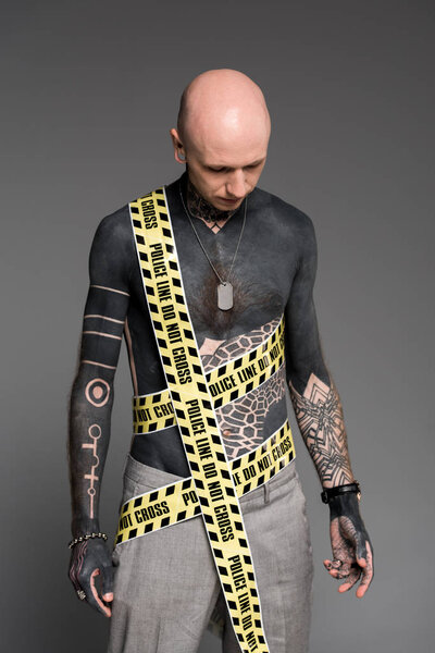 bald shirtless tattooed man with police line around body looking down isolated on grey 