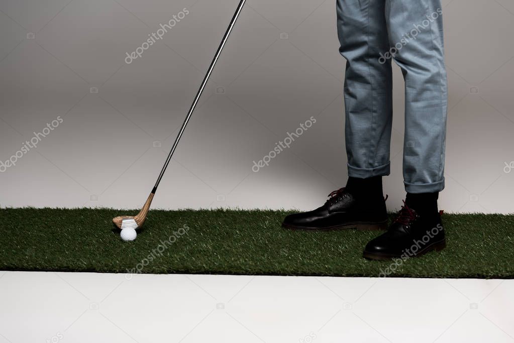 low section of man in jeans and leather boots playing golf on artificial grass on grey