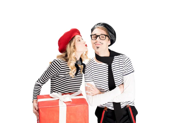 french man standing with crossed arms while attractive woman holding gift box and kissing cheek isolated on white