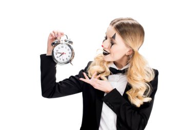 cheerful female clown looking at alarm clock isolated on white 