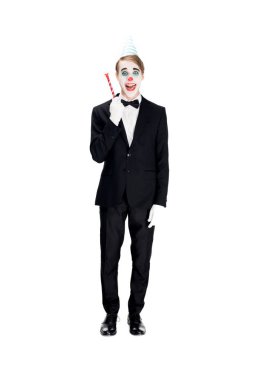 cheerful clown in suit and birthday cap holding blower isolated on white  clipart