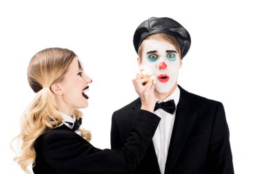 cheerful female clown throwing cupcake in face of surprised man isolated on white  clipart