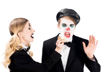 cheerful female clown throwing cupcake in face of dissatisfied man isolated on white  clipart