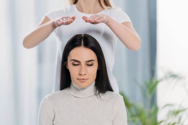 cropped shot of young woman with closed eyes sitting and receiving reiki healing therapy above head  clipart