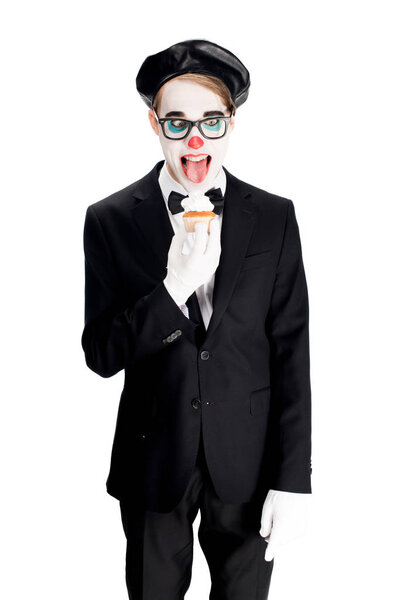 crazy clown in suit showing tongue while eating cupcake isolated on white 