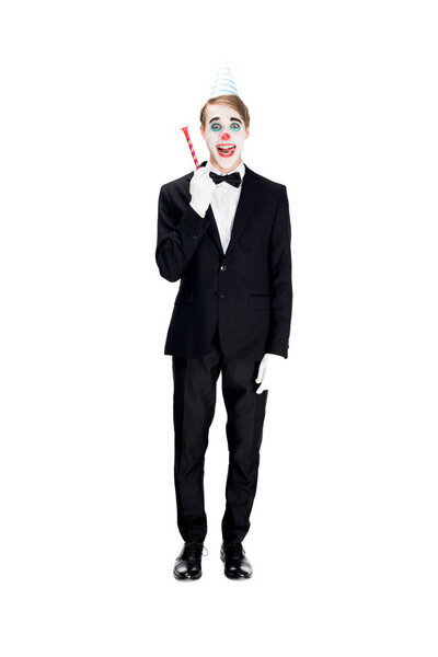 cheerful clown in suit and birthday cap holding blower isolated on white 