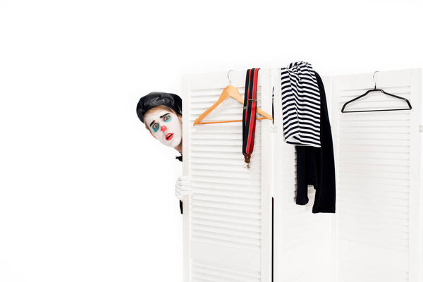 клоун в черном берете, выглядывающий из раздевалки, изолированной на белом
 