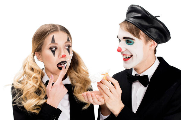 smiling clown looking at woman with cupcake on face licking off sweet finger isolated on white 