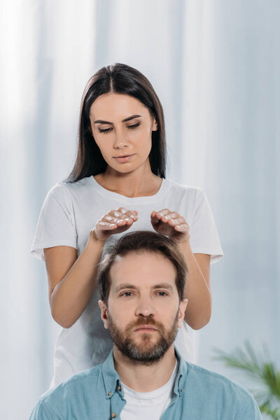 calm man looking at camera while receiving reiki treatment from young female healer 