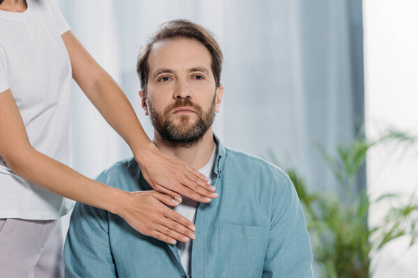 cropped shot of bearded man sitting and receiving reiki treatment on chest