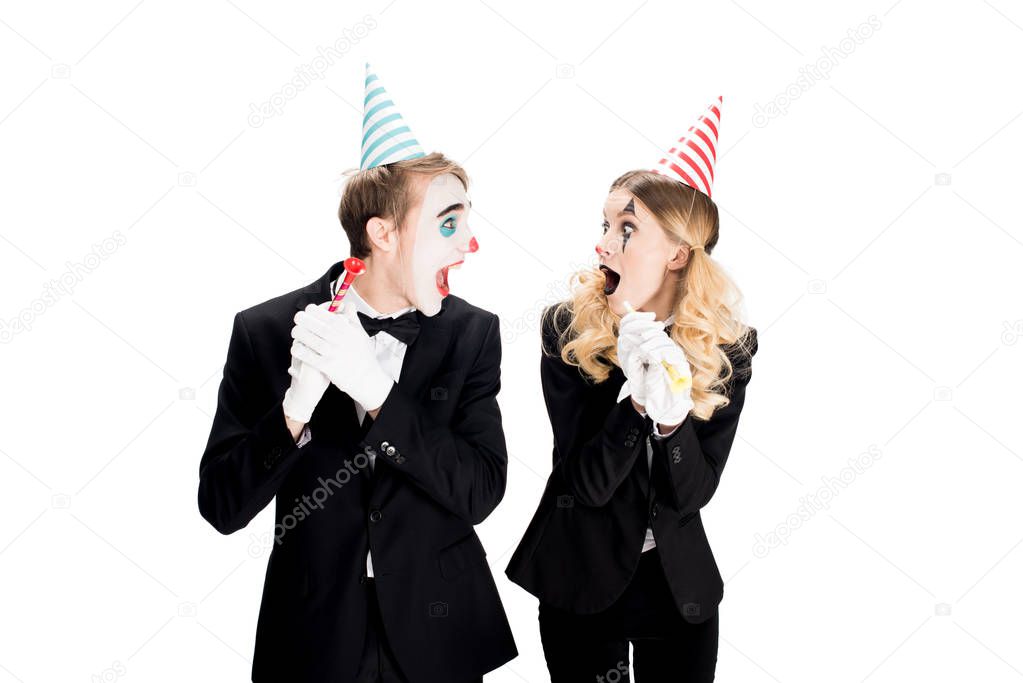 couple of clowns in suits looking at each other and holding birthday blowers isolated on white 