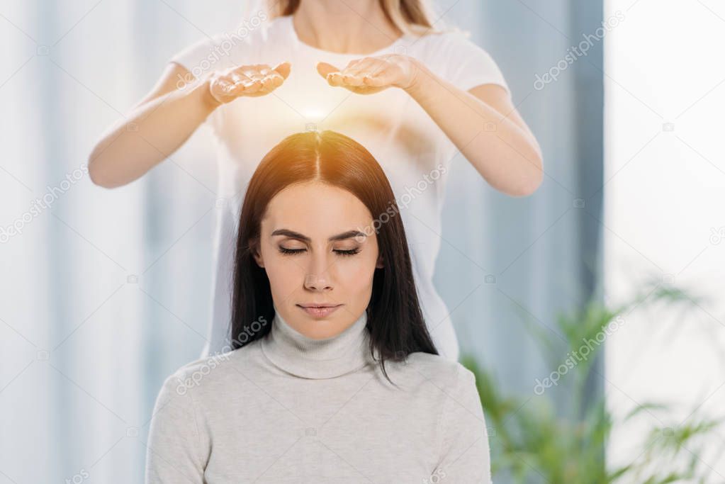 peaceful young woman with closed eyes receiving reiki healing therapy above head 