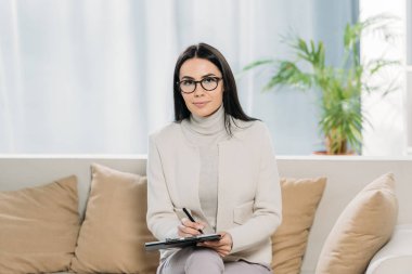 panoya yazma ve kameraya gülümseyen Gözlük Genç kadın psikolog
