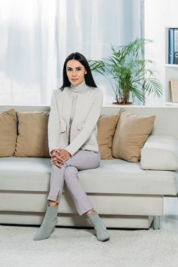 kanepede oturan ve kameraya gülümseyen güzel genç kadın görünümünü tam uzunlukta 