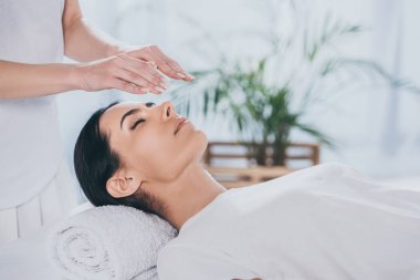 cropped shot of calm young woman with closed eyes receiving reiki treatment above head clipart