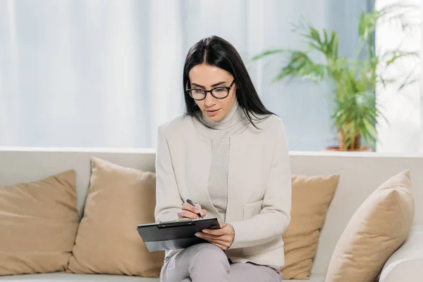 Jonge Vrouwelijke Psycholoog Brillen Zittend Bank Schrijven Klembord — Stockfoto