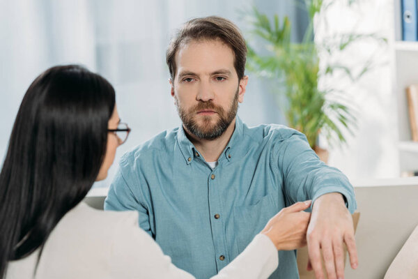 молодая женщина в очках держит за руку бородатого мужчину во время гипнотерапии
