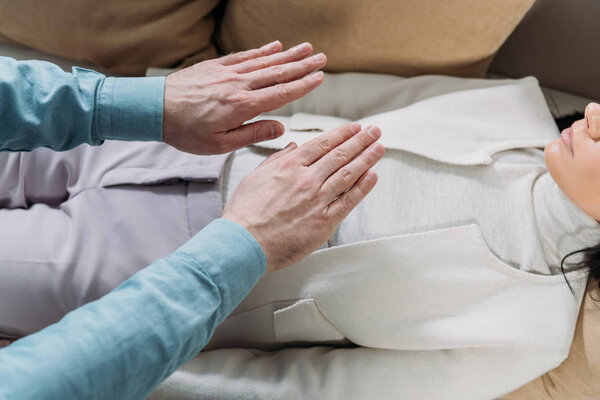 cropped shot of man doing reiki healing therapy to young woman lying on couch