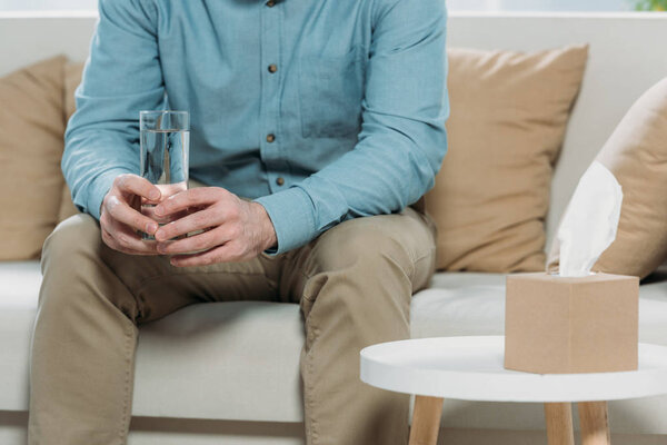 cropped shot of man holding glass of water while sitting on couch in psychotherapist office