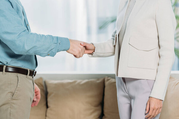 cropped shot of psychotherapist and patient shaking hands in office