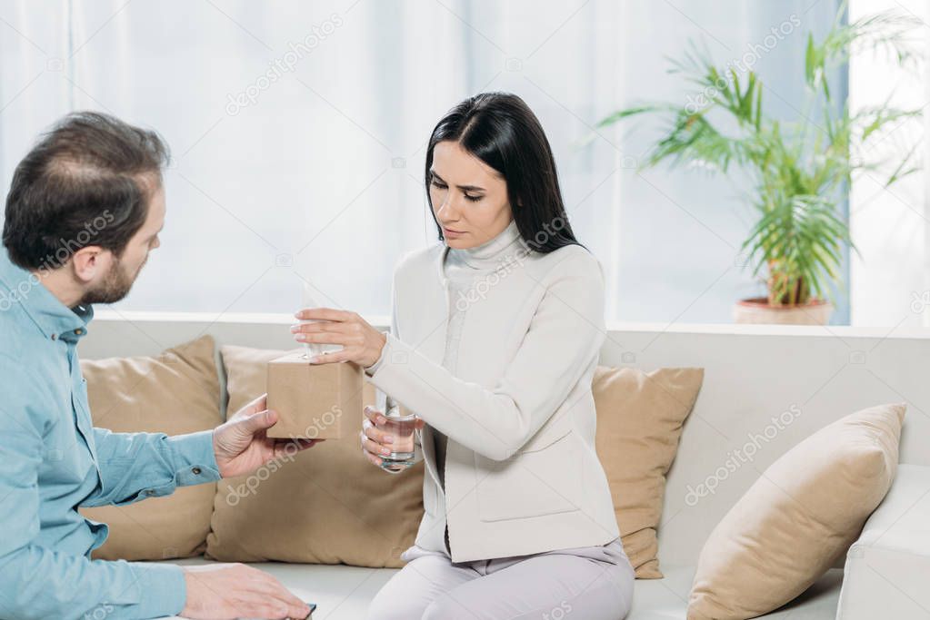psychotherapist with clipboard giving paper tissues to upset young patient with glass of water 